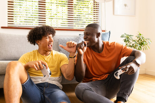 At home, Playing video games, two diverse male friends laughing and enjoying time together indoors