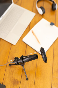 At home, Podcasting setup with microphone, laptop, headphones, and notepad on wooden table