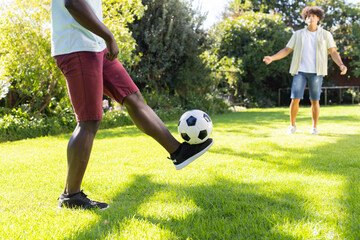 Playing soccer in backyard, two diverse male friends enjoying outdoor activity together