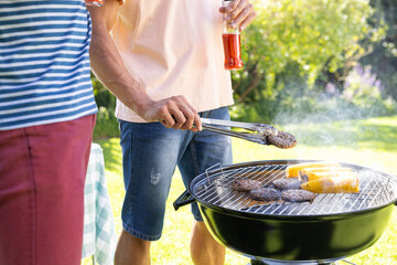 Grilling burgers and corn, two diverse male friends enjoying outdoor barbecue with drinks
