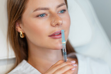 Beautiful doctor cosmetologist woman with clear skin of face holds filler injection near sexy lips...
