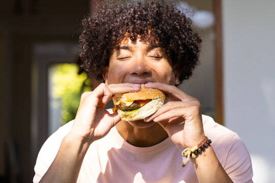 Enjoying delicious burger, man savoring every bite while sitting outdoors