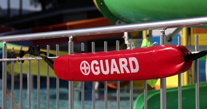 Red tube with word Guard printed on side for rescuing drowning people on fence by pool with slides. Hotel swimming safety measures