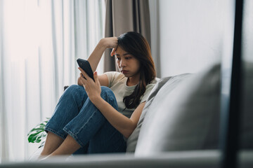 Fototapeta premium Unhappy lonely depressed woman is sitting on the couch and using a phone.