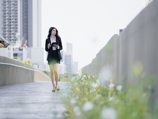 Obraz premium Confident businesswoman in black suit walking outdoors in downtown district street to office holding digital tablet. Smart and beautiful woman in well-dressed jacket walk outside in urban. copy space.