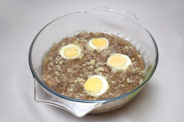 aspic jelly with boiled meat pieces and halved eggs. frozen bone broth in glass round saucepan