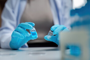 Scientist in Laboratory Holding Vials with Blue Liquid, Wearing Protective Gloves and Lab Coat, Conducting Research