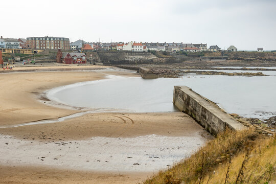 long exposure image of North Sea and bay at Cullercoats Newcastle England with castle ruin, cliff, promenade beach and people swimming in ocean