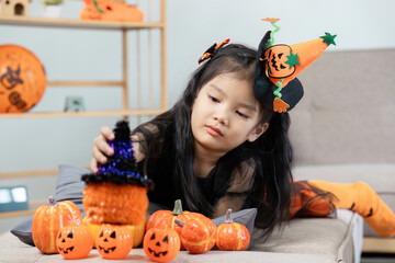 Fototapeta premium Adorable Child in Halloween Costume Playing with Pumpkin Decorations Indoors
