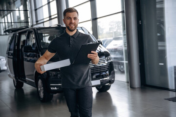 Business of delivery, with notepad. Man loader is near the car with a box