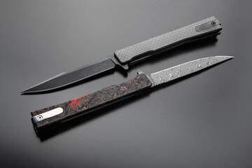 Two pocket folding knives with decorative handles on a dark surface, one open and one closed,...