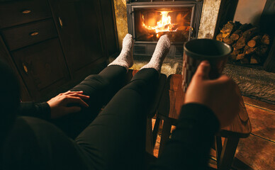 Legs view of woman wearing warm socks while drinking hot tea in front of fireplace - Winter...