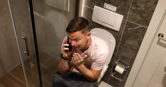 Man talks on phone telling about situation secretly hiding in toilet premise of apartment. Concept of unexpected call and uncomfortable position slow motion