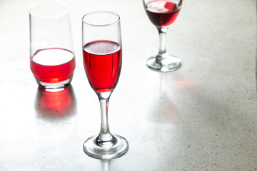 Three glasses filled with red wine sit on a terrazzo textured granite table with one of the red tulip beer glasses standing out in the middle