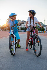 Fototapeta premium Two confident youngsters enjoy a bike ride in the city, showcasing their friendship and joy. The image highlights health, vitality, and the importance of safety measures like wearing helmets.