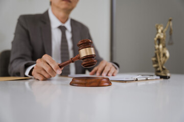 Judge's Gavel and Legal Documents: Close-up of a judge's hand holding a gavel, legal documents, and the statue of Lady Justice in the background.  A symbol of justice and the legal process. 