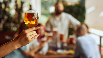 Fan holding beer glass, setting mood for game. The blurred backdrop adds to the sense of camaraderie among fans. Concept of Oktoberfest, alcohol drinks, brewery, vacation, Friday mood.