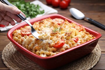 Woman eating delicious al forno pasta at wooden table, closeup