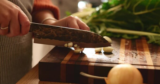 Hands, kitchen and woman chop garlic for cooking healthy dinner, meal or culinary food at home. Knife, ingredients and closeup of female chef cut vegetables for diet, nutrition or wellness supper.