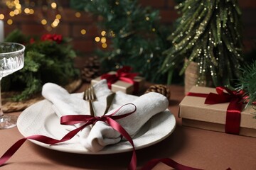Christmas place setting with plate, napkin, cutlery and festive decor on brown table, closeup