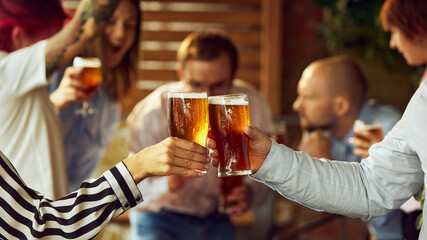 Lively gathering of sport fans, red cups and beer abound, as glasses meet in center. Joy of competition and camaraderie evident all around. Concept of Oktoberfest, brewery, vacation, Friday mood.