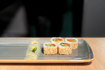 Close-up of the chef serving a rectangular dish of sushi in sesame seeds with fish, rice, cucumbers, nori before serving to the guests.