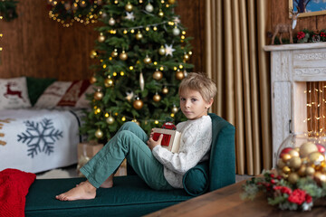 Sweet blond child, cute boy, playing with christmas toys on Christmas, beautifully decorated home for Christmas, cosy place