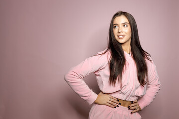 Obraz premium Young woman in a pink tracksuit on a pink background. Brunette, tanned, model.