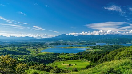 Obraz premium An elevated view from Kurumayama Plateau on a clear day, showing off the vibrant greenery and the shimmering Lake Shirakaba in the distance.