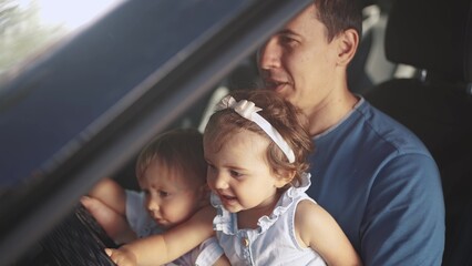 dad plays with children in the car. people family and children concept. two beautiful little kids sit on their father's lap and turn the steering wheel of his car lifestyle