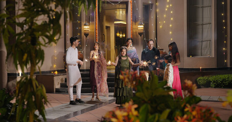 Obraz premium Indian Hindu Asian happy family teen girl boy child hold play crackers make fun joy night decor light diya home young adult male man female wife lady multi group older elder mom dad enjoy Diwali house