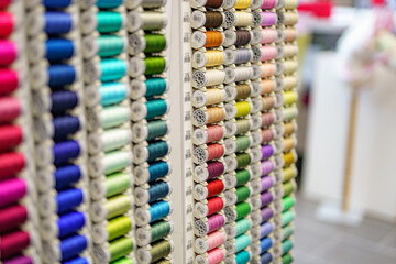 Close-up of colored sewing threads of different colors on display in a sewing shop. It is multicolored and made of textile sewing threads.