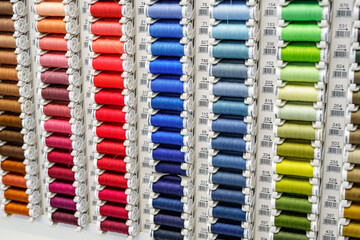 Close-up of colored sewing threads of different colors on display in a sewing shop. It is multicolored and made of textile sewing threads.