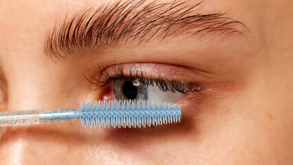 Close-up of a woman's eyelashes being brushed with wand, focusing on makeup application, and...