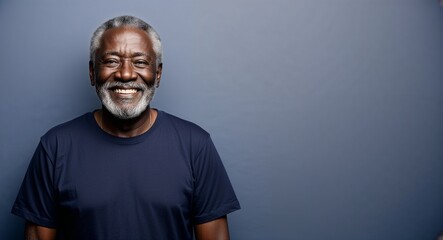 Obraz premium Smiling elderly Black man with grey beard wearing tshirt on plain navy blue background