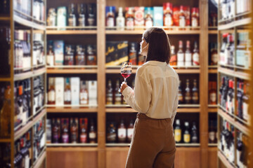 Woman sommelier at wine cellar full of bottles with exquisite alcohol drinks, that have various sweet and sour tastes and dates of manufacture on large wooden shelves.