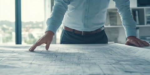 Businessman analyzing blueprint details on a table in a modern office, showcasing planning and strategy in urban development.