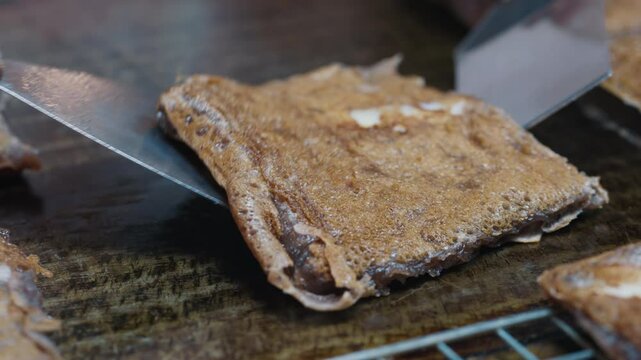 Equipped with utensils person cooking and turning over on hot pan sweet thai coconut pancakes khanom babin square shape. Traditional asian street food with glutinous rice flour and chewy filling.