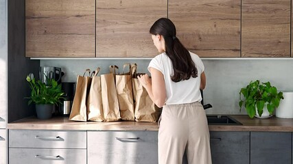Young woman next to paper bags full of food in kitchen. Groceries ordered online and delivered by courier