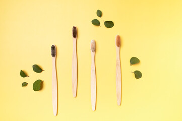 Bamboo wooden eco toothbrushes and green leaves on yellow background top view. Eco-friendly hygiene...