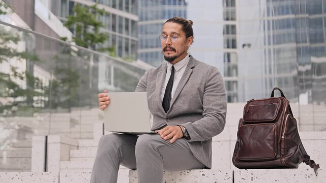Man Caucasian male trying to make his laptop to work while sitting on staircase outside. Pressing small button multiple times. Closing laptop lid with anger. Gadget not responding and not functioning.