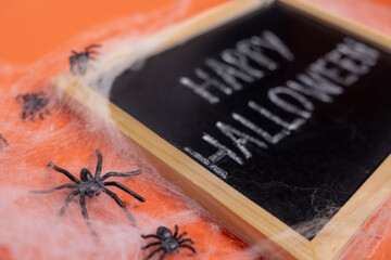 A blackboard with the words “Happy Halloween” on an orange background. Spiders making a web