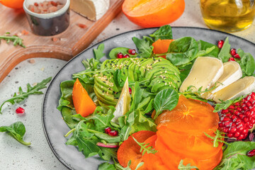 vitamin winter salad with persimmons, fresh greens, avocado, Camembert cheese and pomegranate. organic healthy products. top view