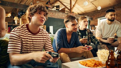 Surrounded by snacks and drinks, friends deep into action. Room pulses with competitive spirit and light-hearted fun. Concept of football fans, sport evens, video games and cybersport.
