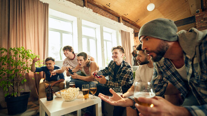 Victory moments and playful shouts bring group of friends closer, enjoying their time together over drinks and some intense gameplay. Concept of football fans, sport evens, video games and cybersport.