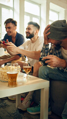 In full swing, everyone's smiles contagious as they compete. Cozy setting with beers and snacks keeps mood friendly and upbeat. Concept of football fans, sport evens, video games and cybersport.