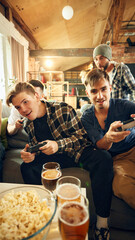 Engaged in intense game, group sits on couch, controllers in hand. Room filled with excitement, snacks within reach, and winning moment close. Concept of football fans, sport evens, cybersport.