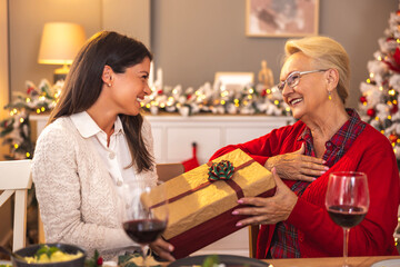 Mother and daughter exchanging Christmas presents while having dinner at home