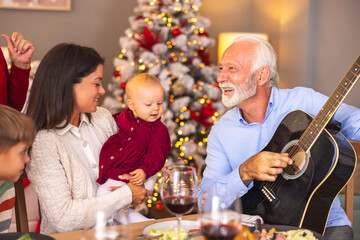 Happy family singing Christmas songs while senior man playing the guitar at home