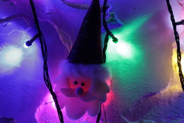 Una toma de cerca de una decoracion de navidad y fin de año con una cara de santa claus  rodeado de varias luces con bombillos de varios colores y bolas de navidad en la oscuridad © Elika R